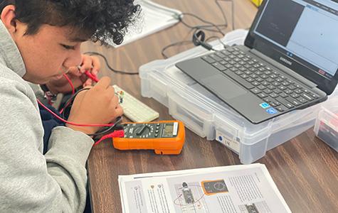 Young student studies instructions while holding wires